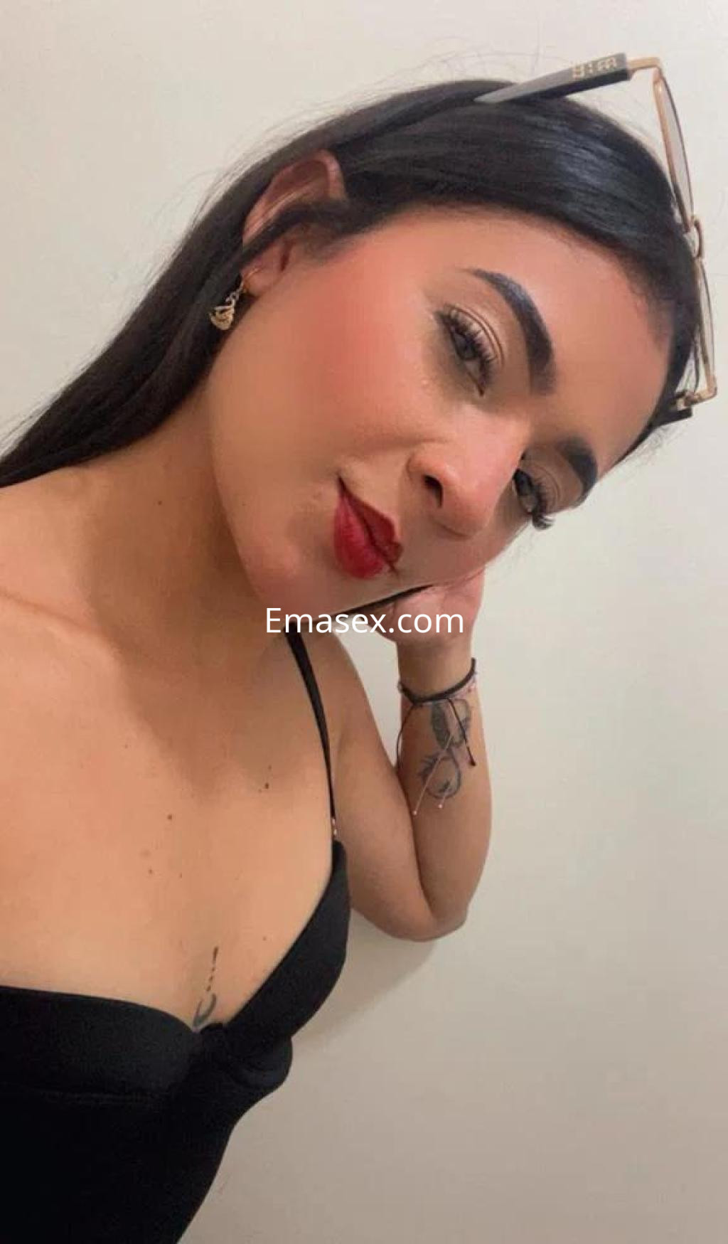 Puta en Cáceres con top negro, luciendo joyería elegante y maquillaje sutil, posando con una mano en su rostro.
