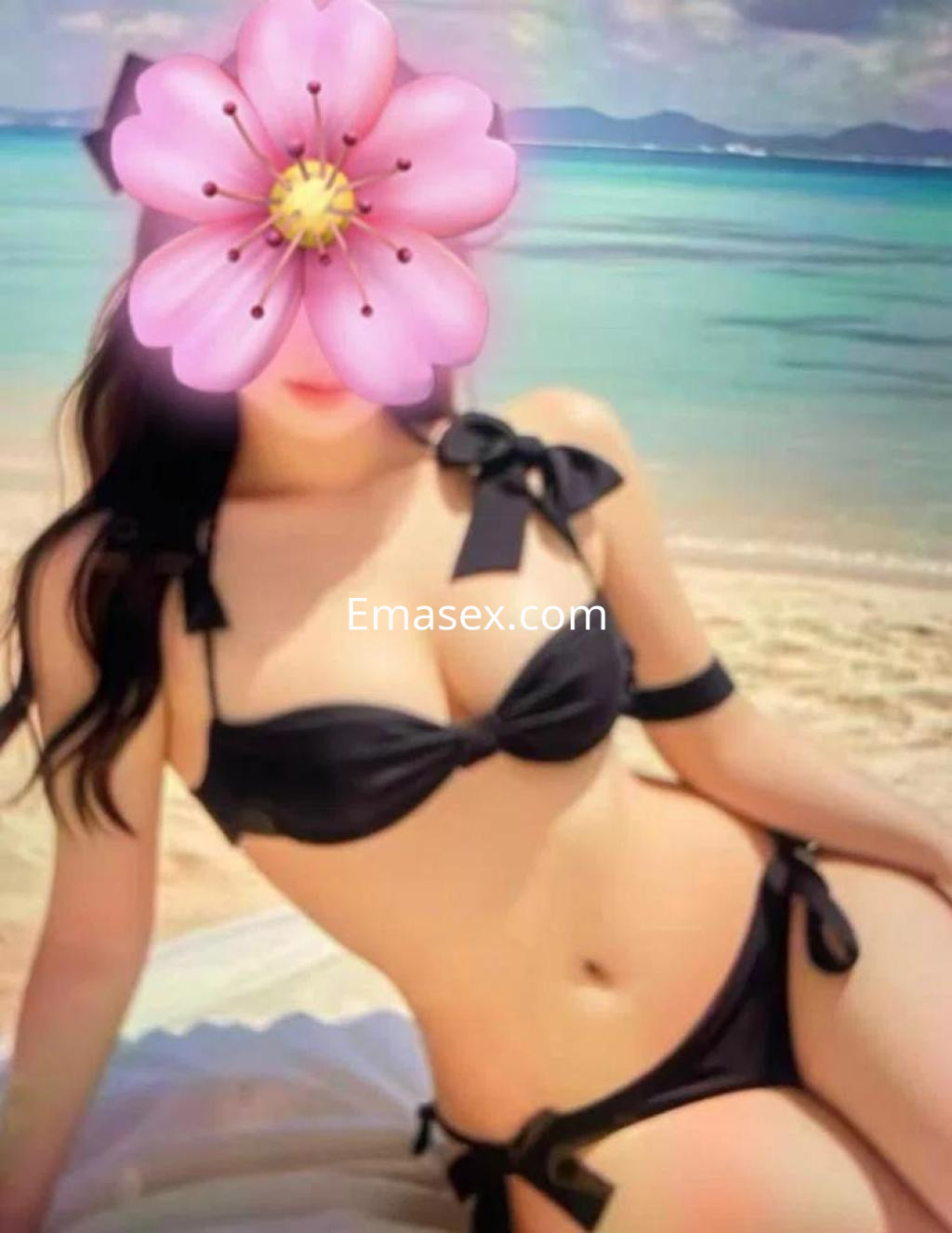 Puta en Castellón, posando en la playa con un bikini negro, sentada sobre una toalla, frente al mar.