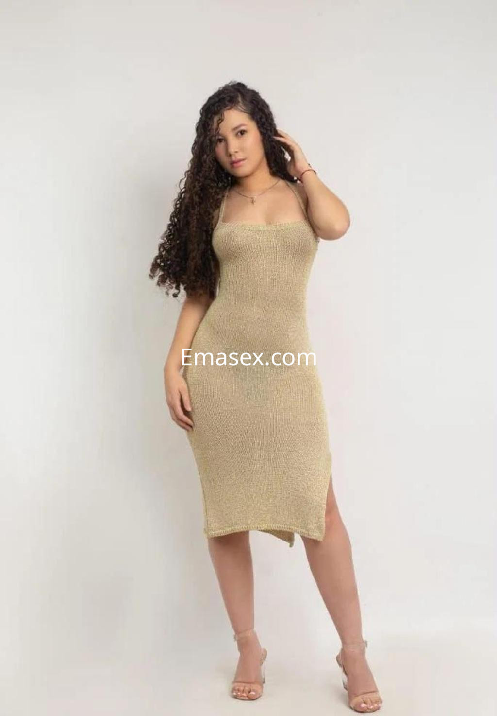 Escort posando en Málaga con un vestido ajustado de color dorado y sandalias, mostrando su cabello rizado.