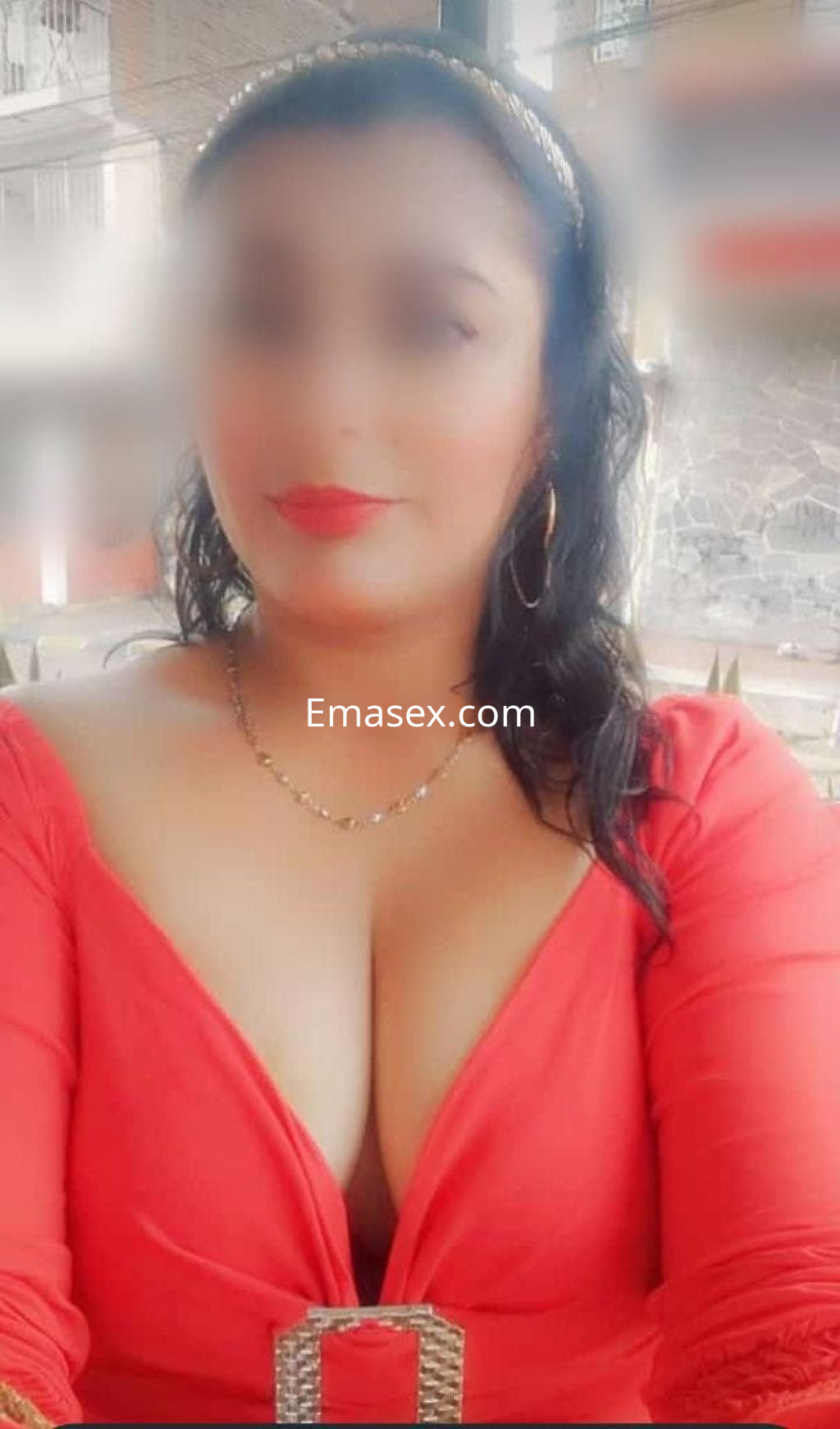 Puta en Murcia luciendo un vestido rojo con escote y accesorios dorados, con cabello oscuro y rizado.