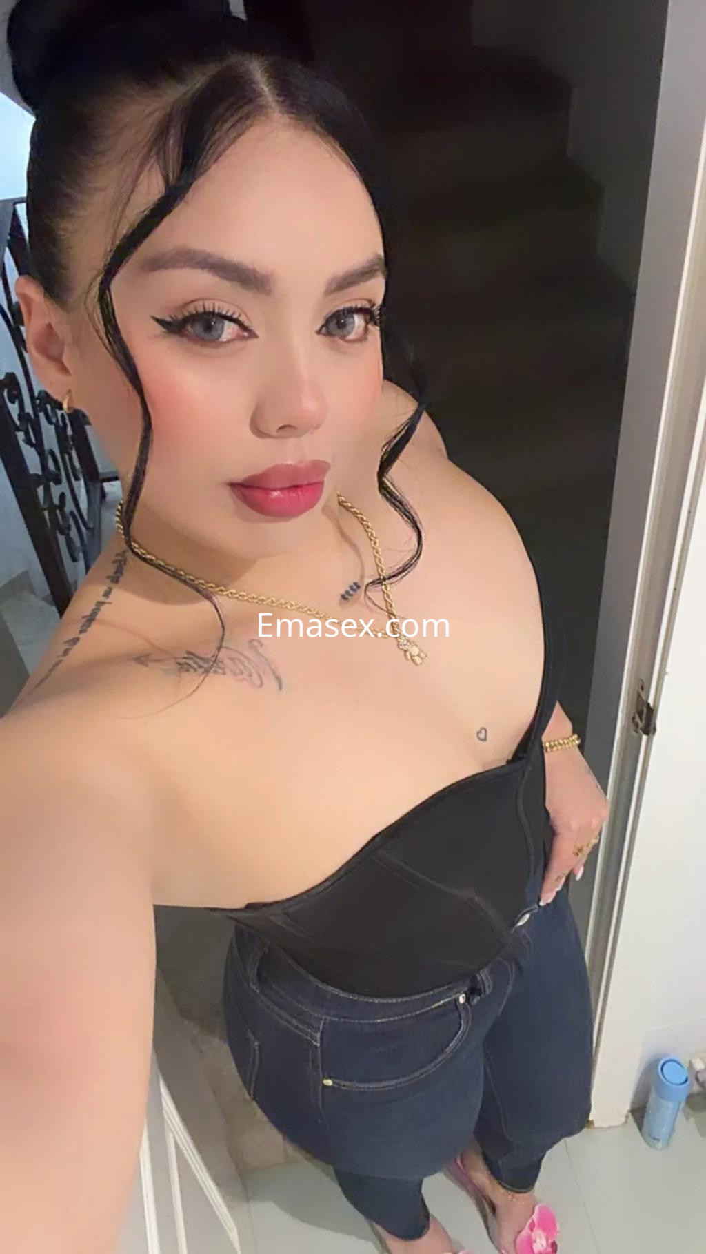 Escort en Murcia con cabello oscuro y lacio, usa un body negro y jeans ajustados, posando en un interior.