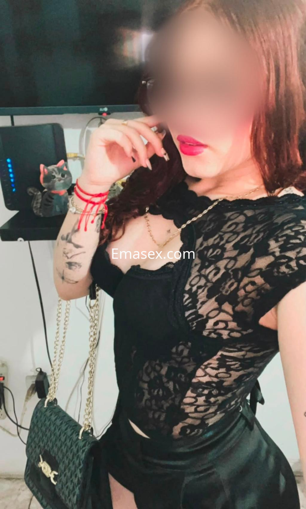 Escort en Pamplona con blusa de encaje negro, labios rojos, y una pose coqueta, mostrando un bolso de mano.