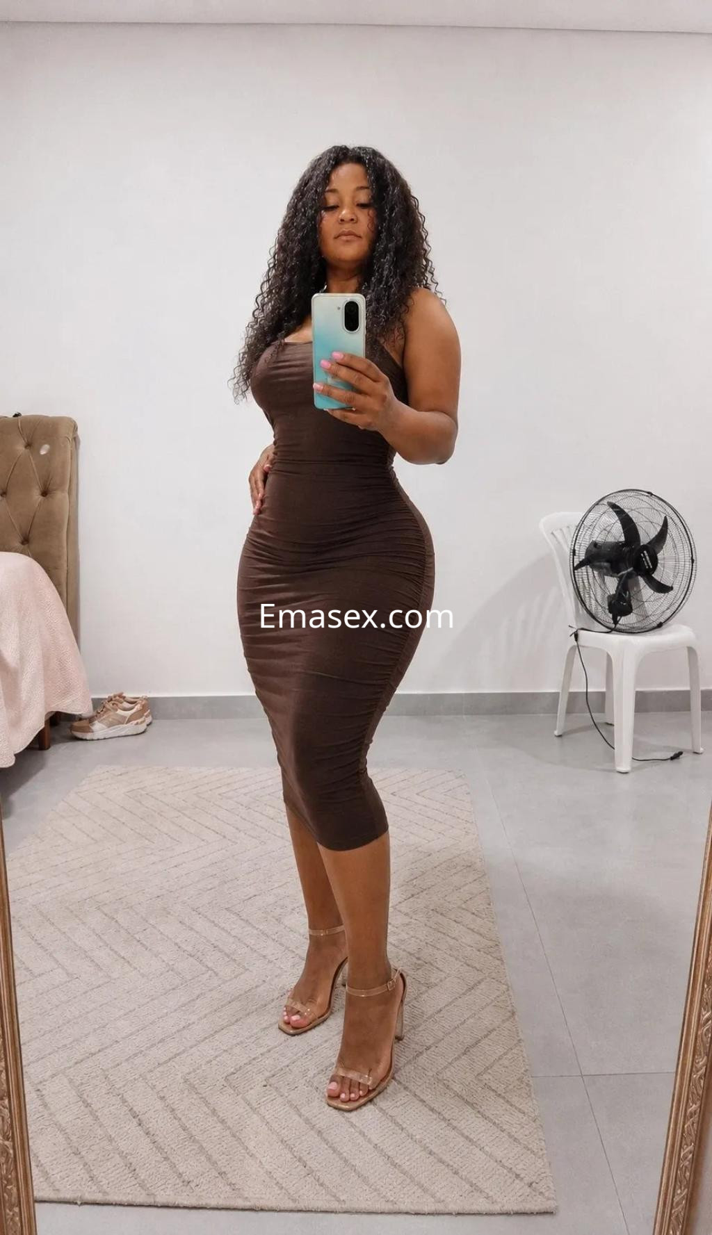 Puta posando frente al espejo con un vestido ajustado marrón, cabello rizado y tacones en Gijón.