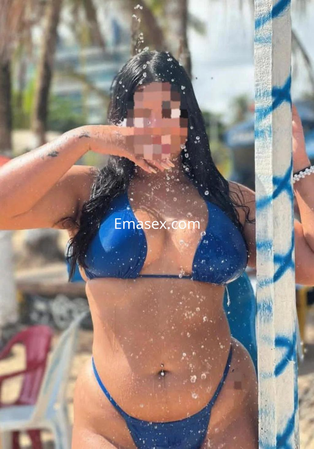 Escort en Las Palmas con bikini azul, posando en la playa mientras el agua salpica alrededor.