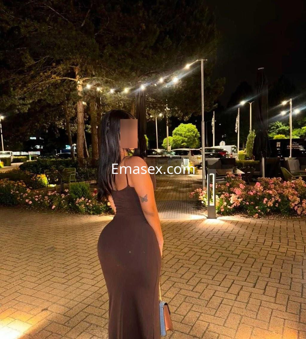 Puta de pie en un entorno al aire libre en Pontevedra, luciendo un vestido negro ajustado y con el cabello largo.