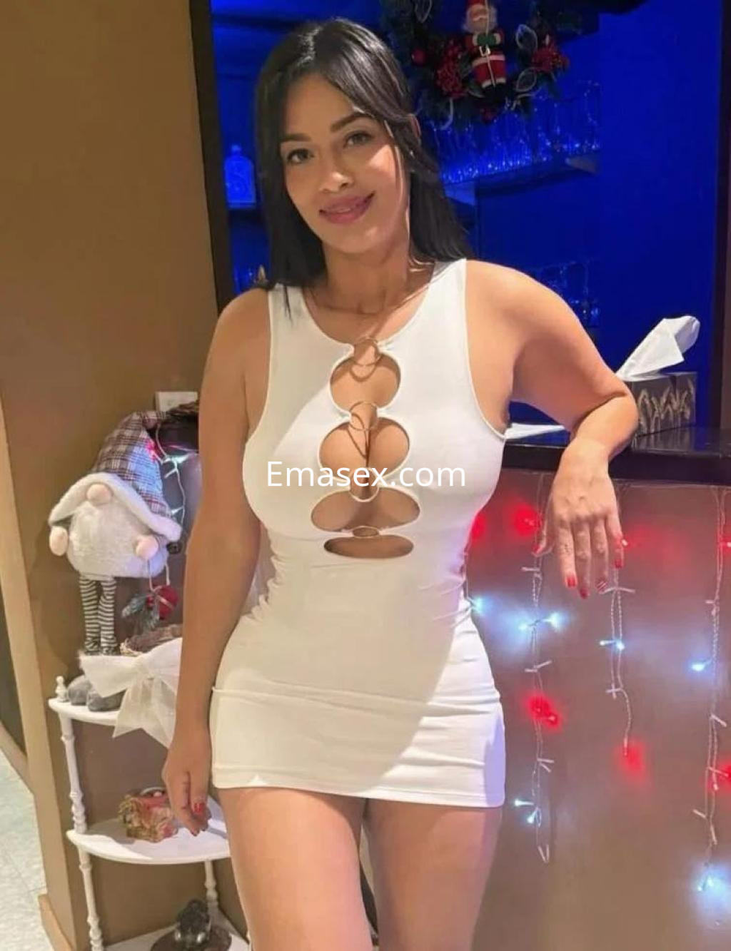 Escort en Pontevedra, con vestido blanco ajustado y detalles en el escote, posando junto a una barra decorada.