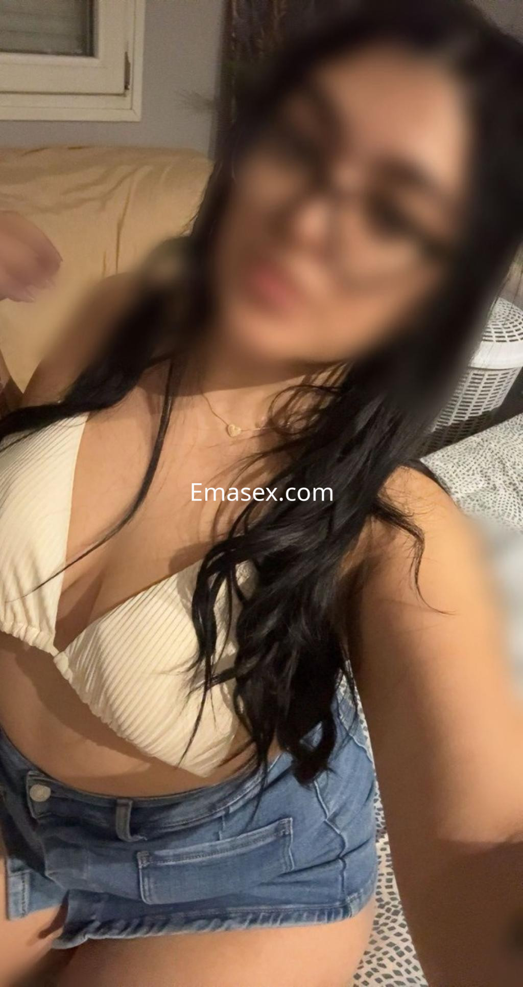 Escort en Salamanca con cabello largo y oscuro, usando un bikini claro y una falda de mezclilla en un entorno interior.