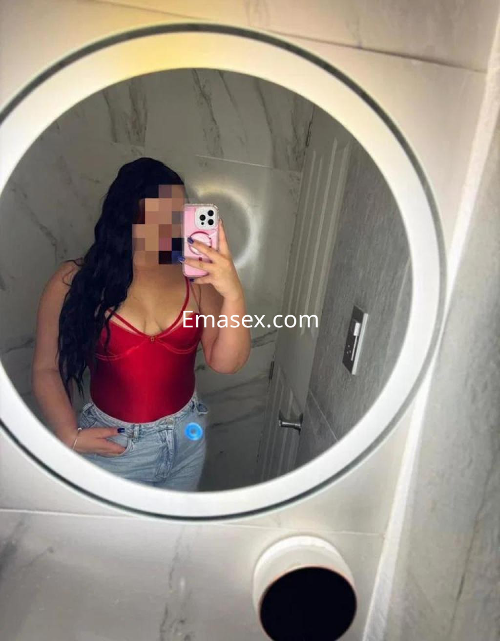 Escort en Sevilla, posando frente a un espejo con un body rojo y jeans, mostrando una actitud segura.