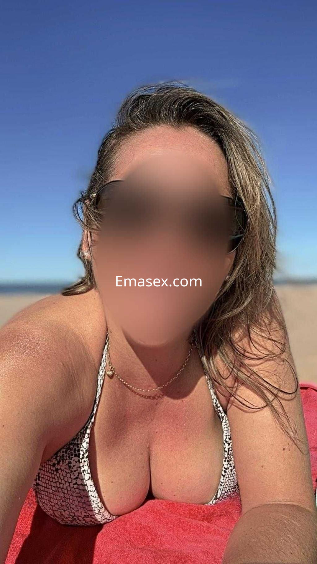 Escort en Tarragona con cabello largo y rubio, usando un bikini de estampado, posando en la playa bajo el sol.