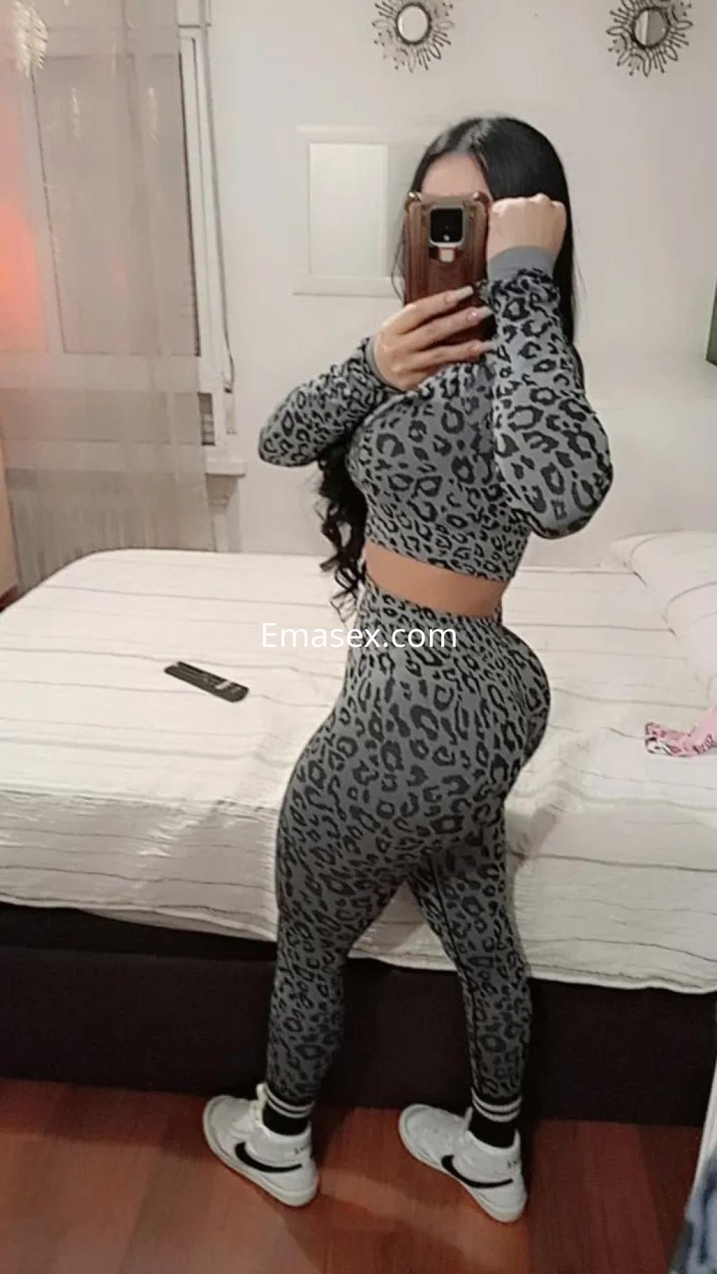 Escort en Valladolid posando de perfil con un conjunto ajustado de estampado de leopardo y zapatillas deportivas.