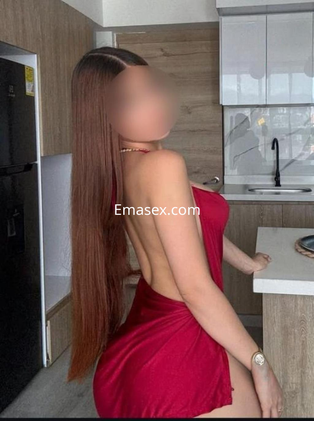 Puta de cabello largo y lacio con un vestido rojo que deja al descubierto un lado de su torso, en una cocina moderna de Valladolid.