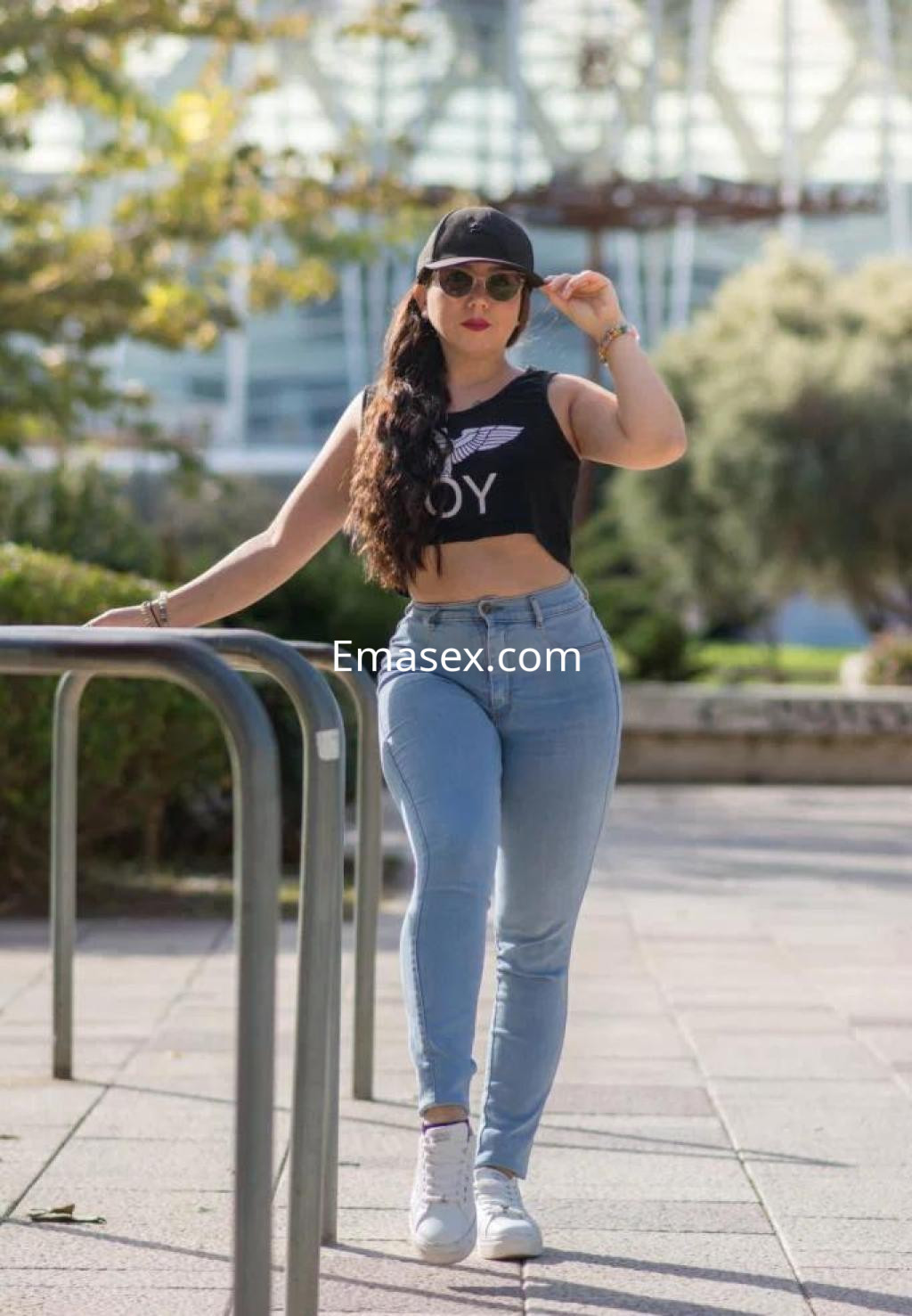 Escort en Zaragoza con cabello largo y trenzado, viste una camiseta negra y jeans ajustados, posando al aire libre.