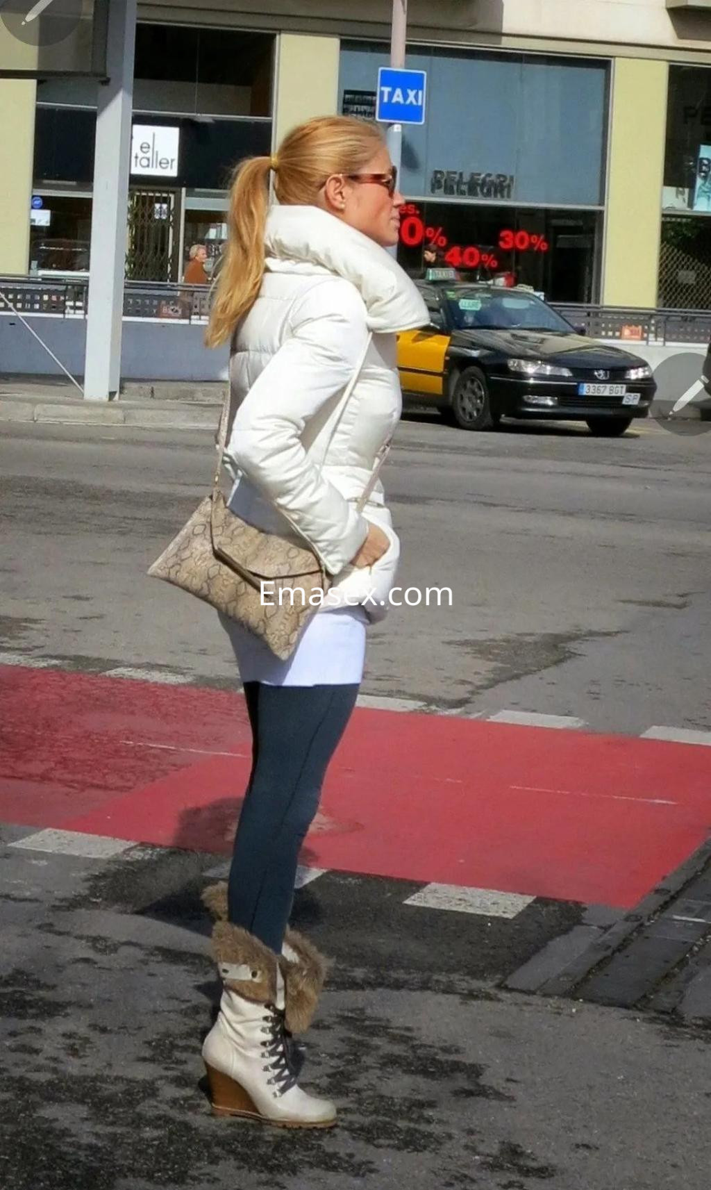 Escort en Zaragoza con abrigo blanco, leggings oscuros y botas de piel, caminando por la calle.