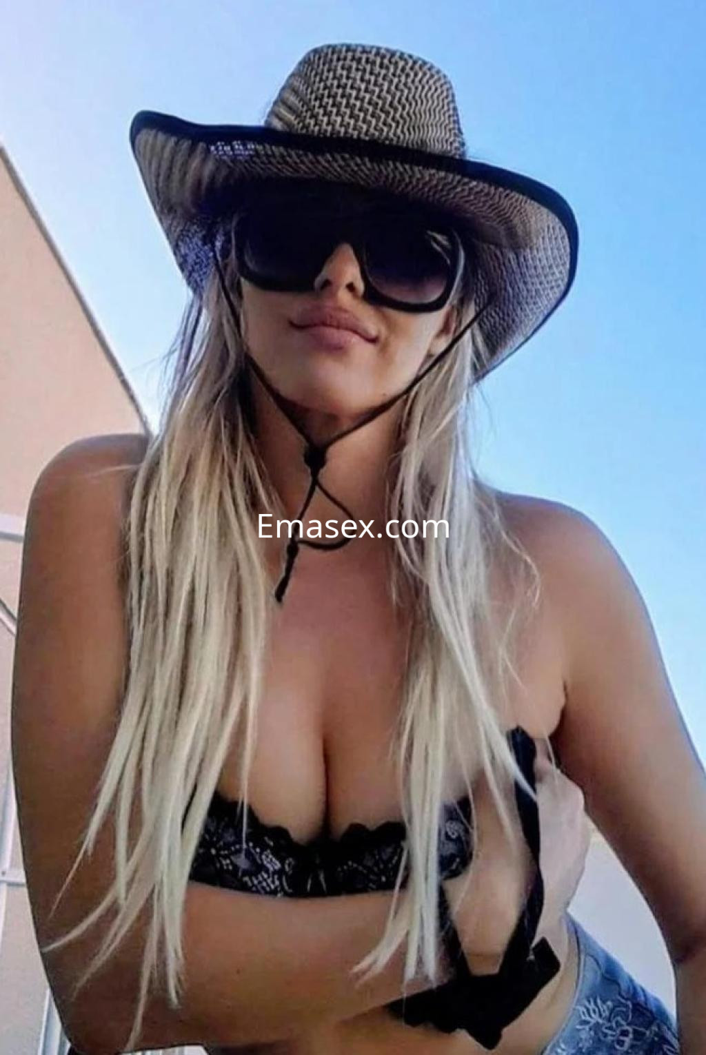 Escort en Almería con cabello largo y rubio, usando un sombrero y gafas de sol, posando al aire libre.