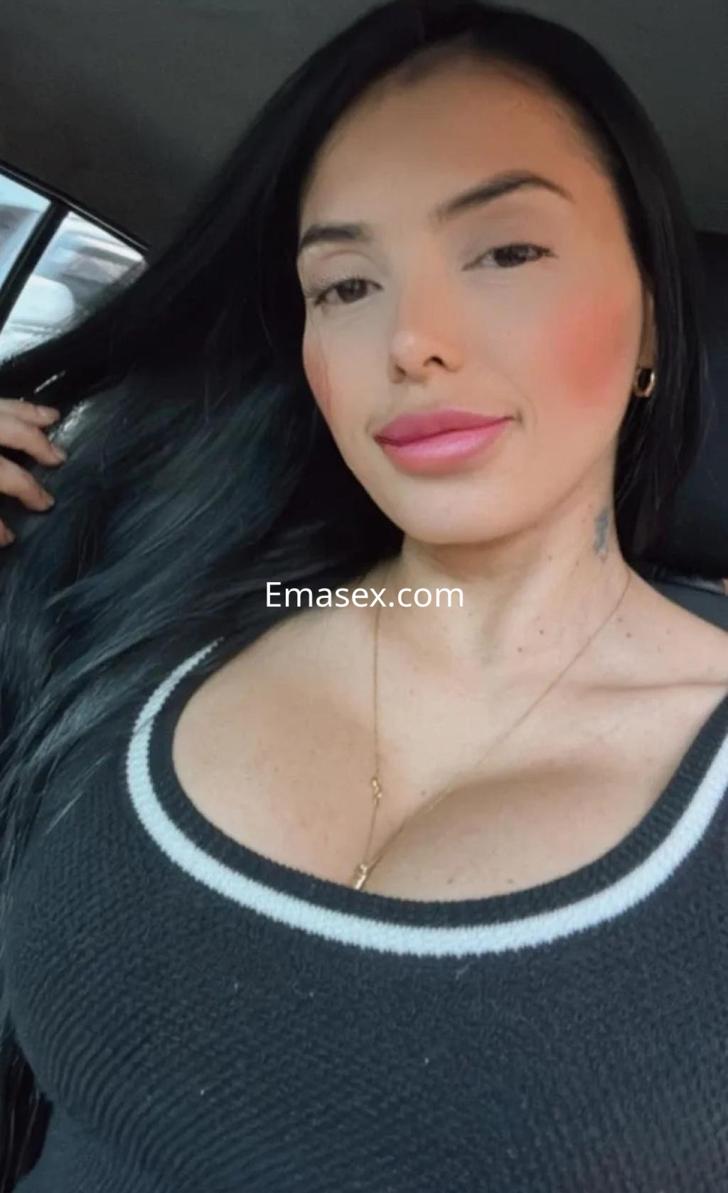 Puta con cabello largo y oscuro, lleva un top negro con detalles blancos, posando en un vehículo en Granada.