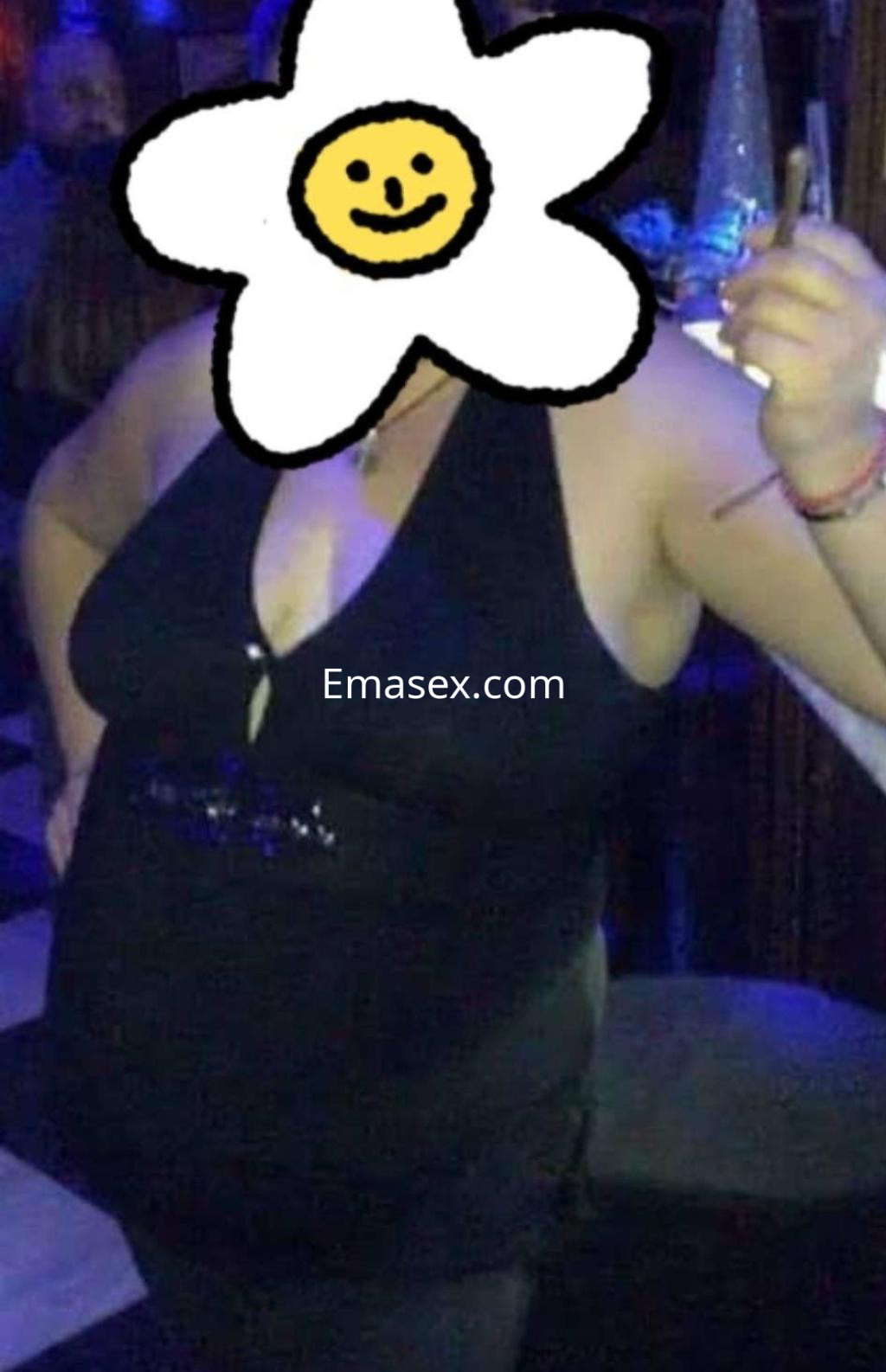 Escort en Granada viste un vestido negro ajustado y se encuentra en un ambiente festivo, sosteniendo un cigarrillo.