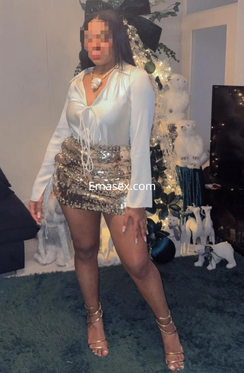Puta de piel morena con blusa blanca y mini falda brillante, posando en una sala decorada en Sevilla.