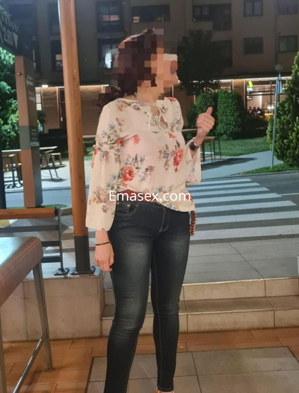 Escort en Madrid con blusa floral y jeans ajustados, posando en un entorno urbano al aire libre.