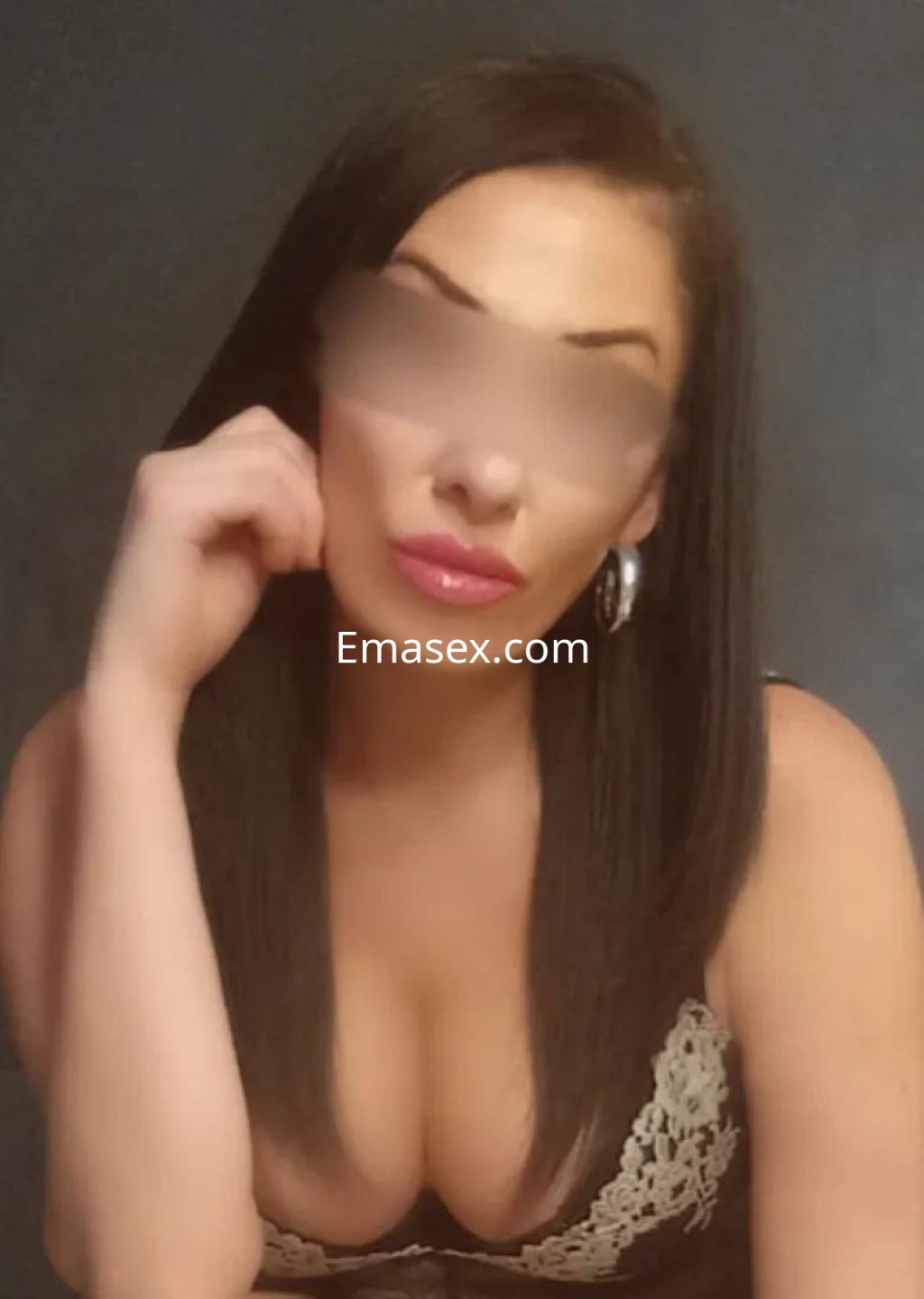 Puta en Sevilla con cabello largo y lacio, luciendo un top de encaje negro y pendiente grande, posando con expresión pensativa.