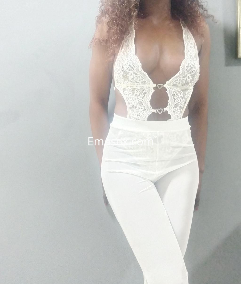 Escort de piel oscura con cabello rizado, vistiendo un conjunto blanco de encaje y pantalones ajustados en Santander.