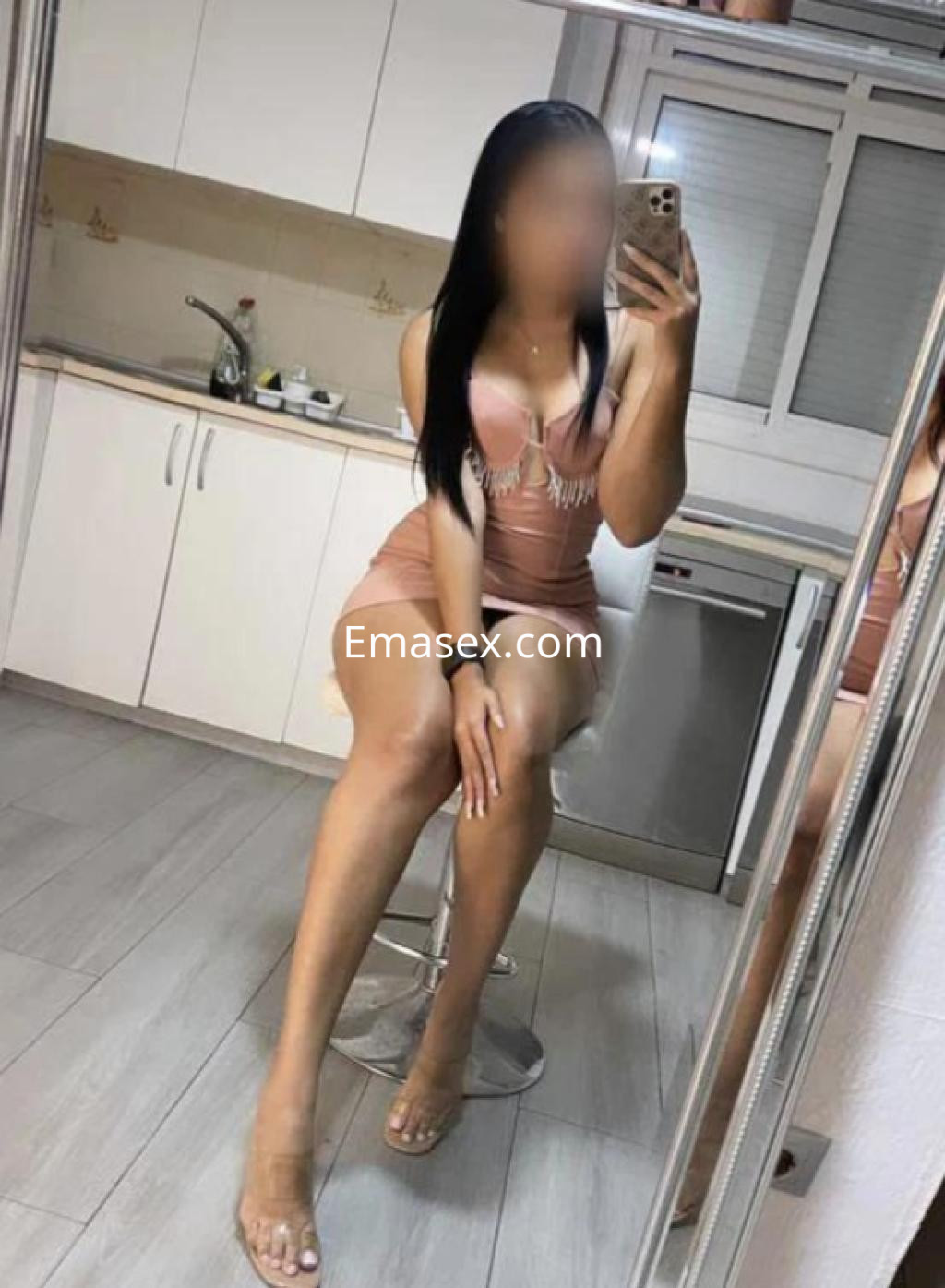 Puta sentada en un taburete en la cocina, viste un vestido corto rosa y sandalias transparentes en Tenerife.
