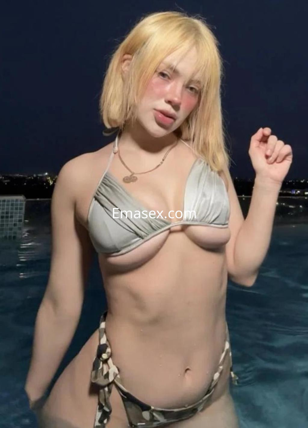 Puta de cabello rubio corto, en bikini claro, posando junto a una piscina en Huelva durante la noche.