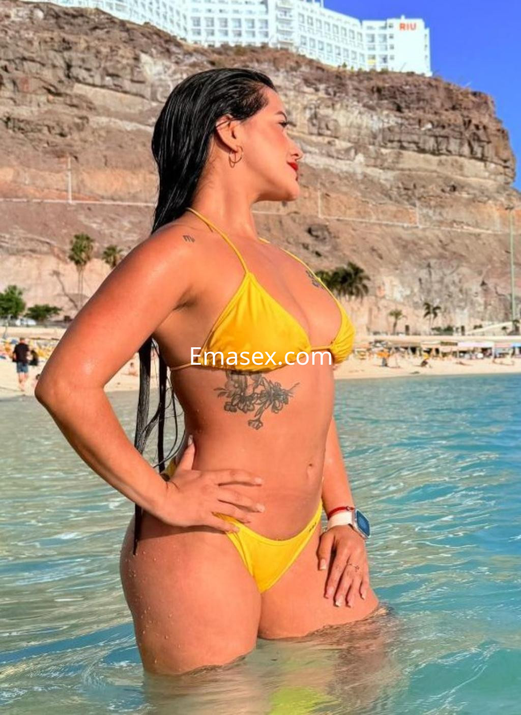 Puta en bikini amarillo posando en el agua cristalina de la playa en Las Palmas, con el cabello mojado y un tatuaje visible.