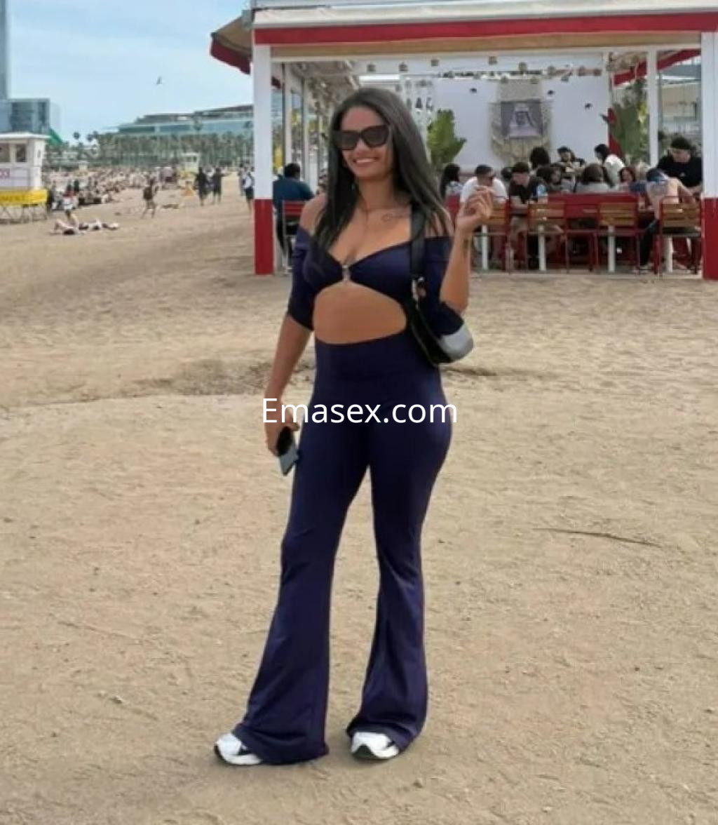 Escort en Barcelona luciendo un conjunto azul oscuro con detalles recortados, posando en la playa.