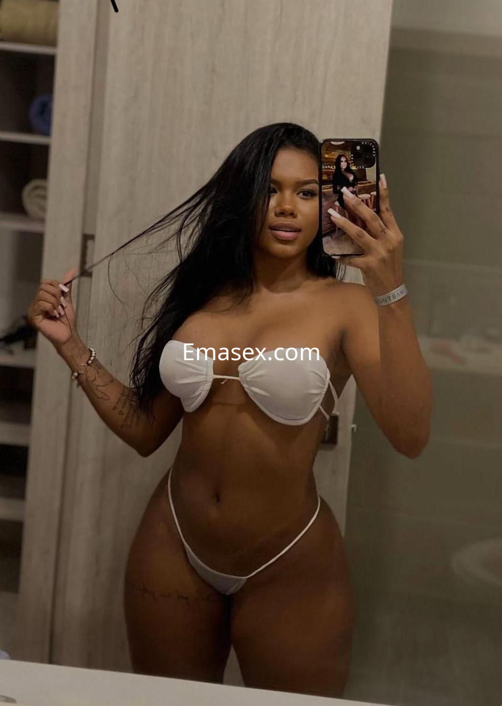 Escort en Tarragona posando en un baño con un bikini blanco, mostrando su cabello largo y lacio.