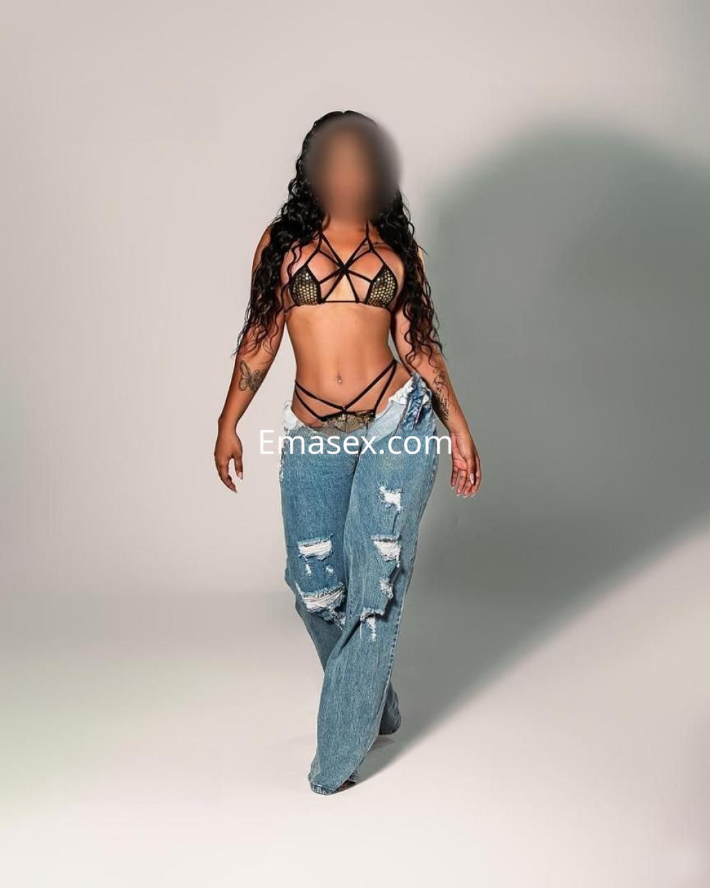 Escort en Albacete con top de tiras negras y vaqueros rasgados, caminando hacia la cámara con cabello rizado.