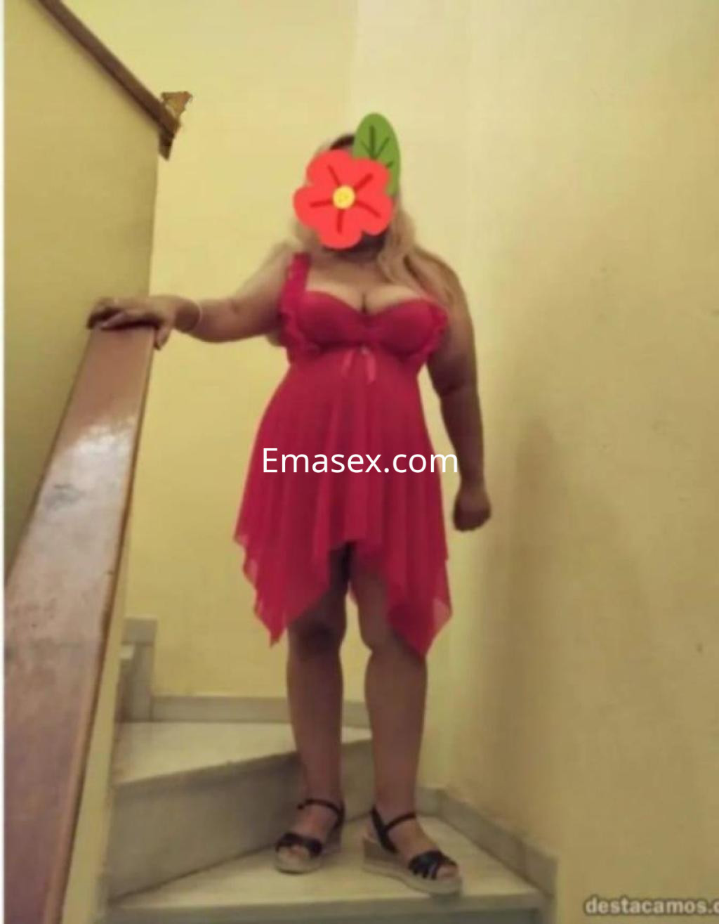 Puta en Almería con cabello rubio, usando un vestido corto rojo transparente y sandalias, posando en una escalera.