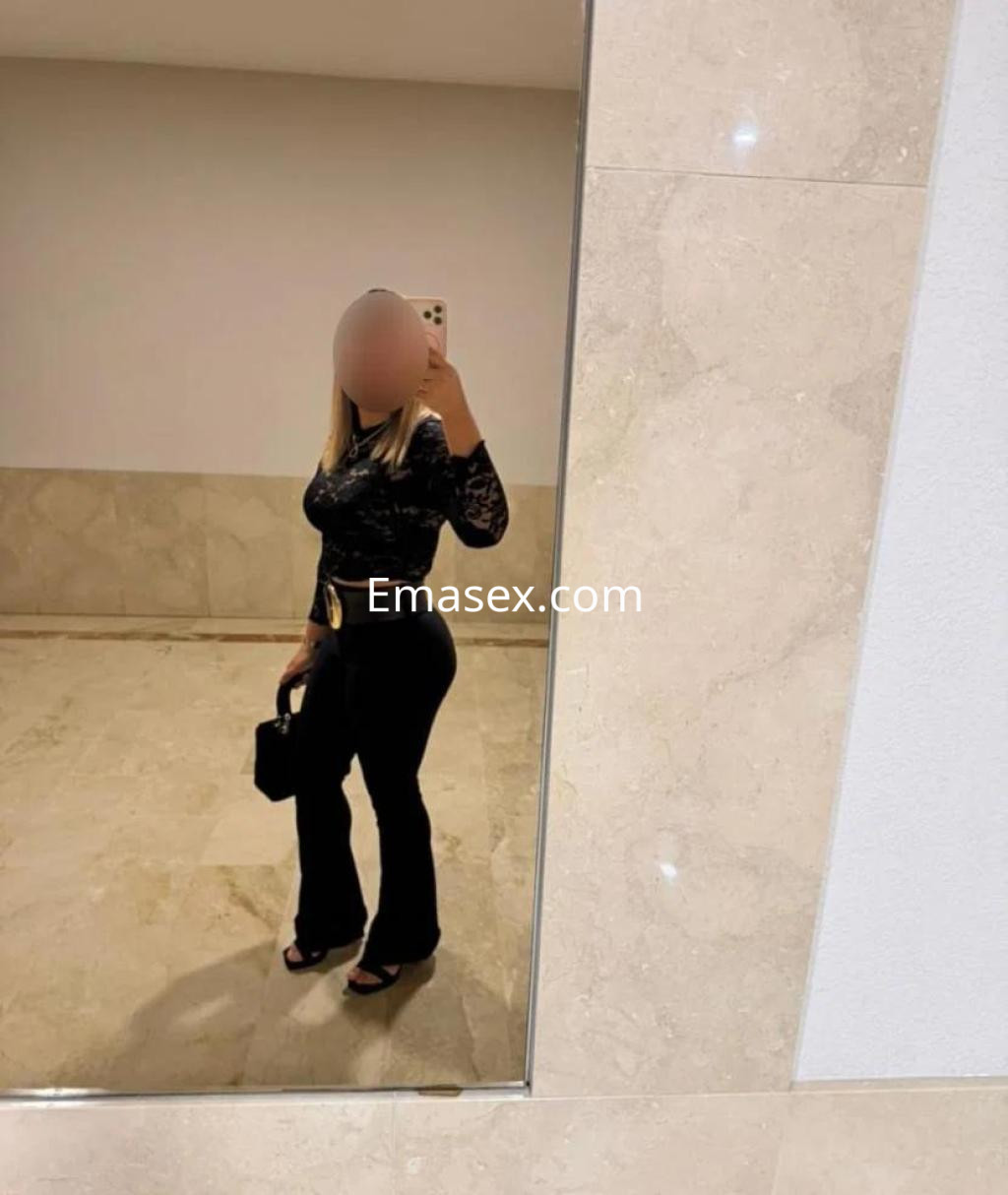 Escort en Badajoz luciendo blusa negra de encaje y pantalones de campana en un ambiente elegante.