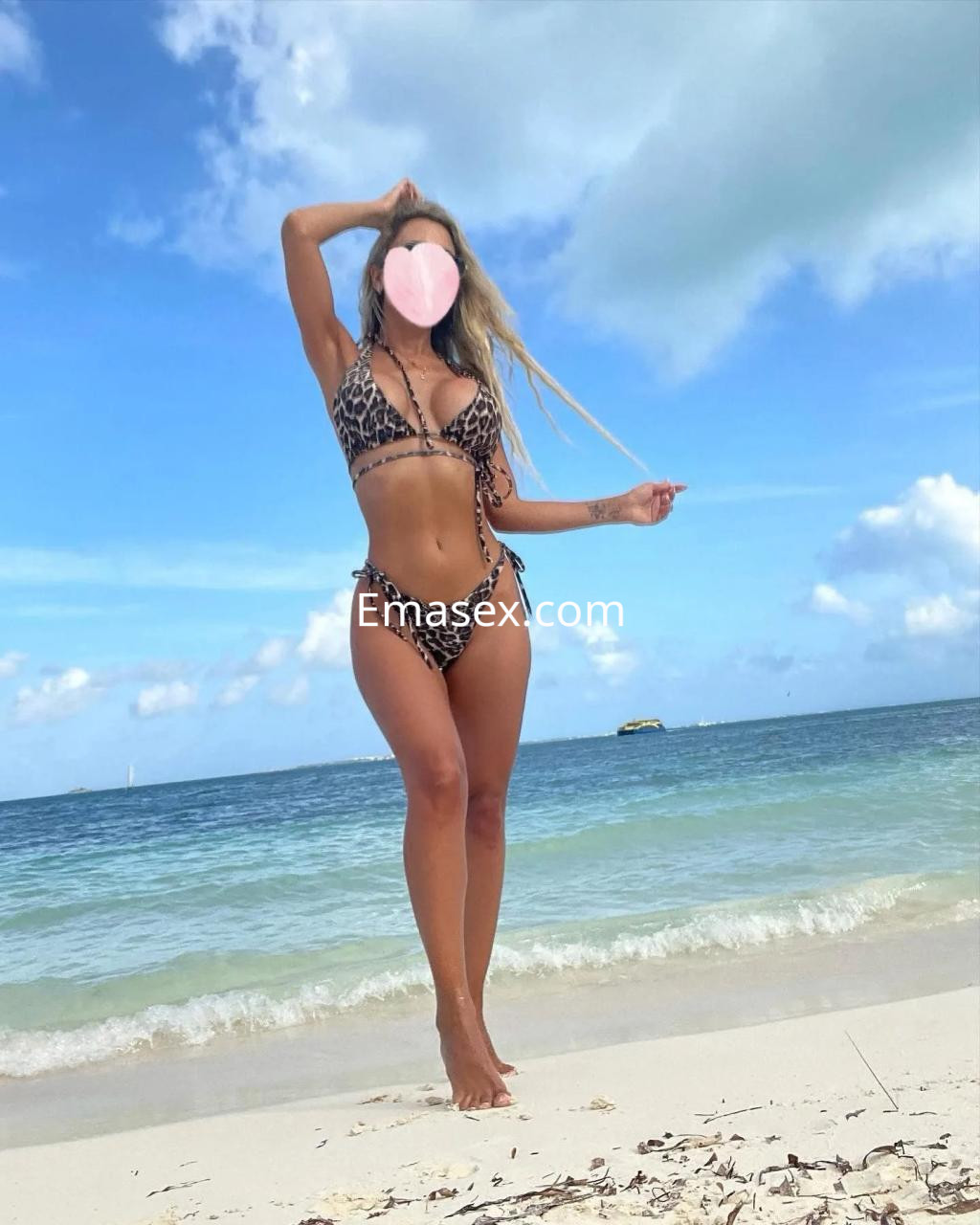 Puta posando en la playa de Palma de Mallorca, con bikini de leopardo y pelo largo, bajo un cielo nublado.