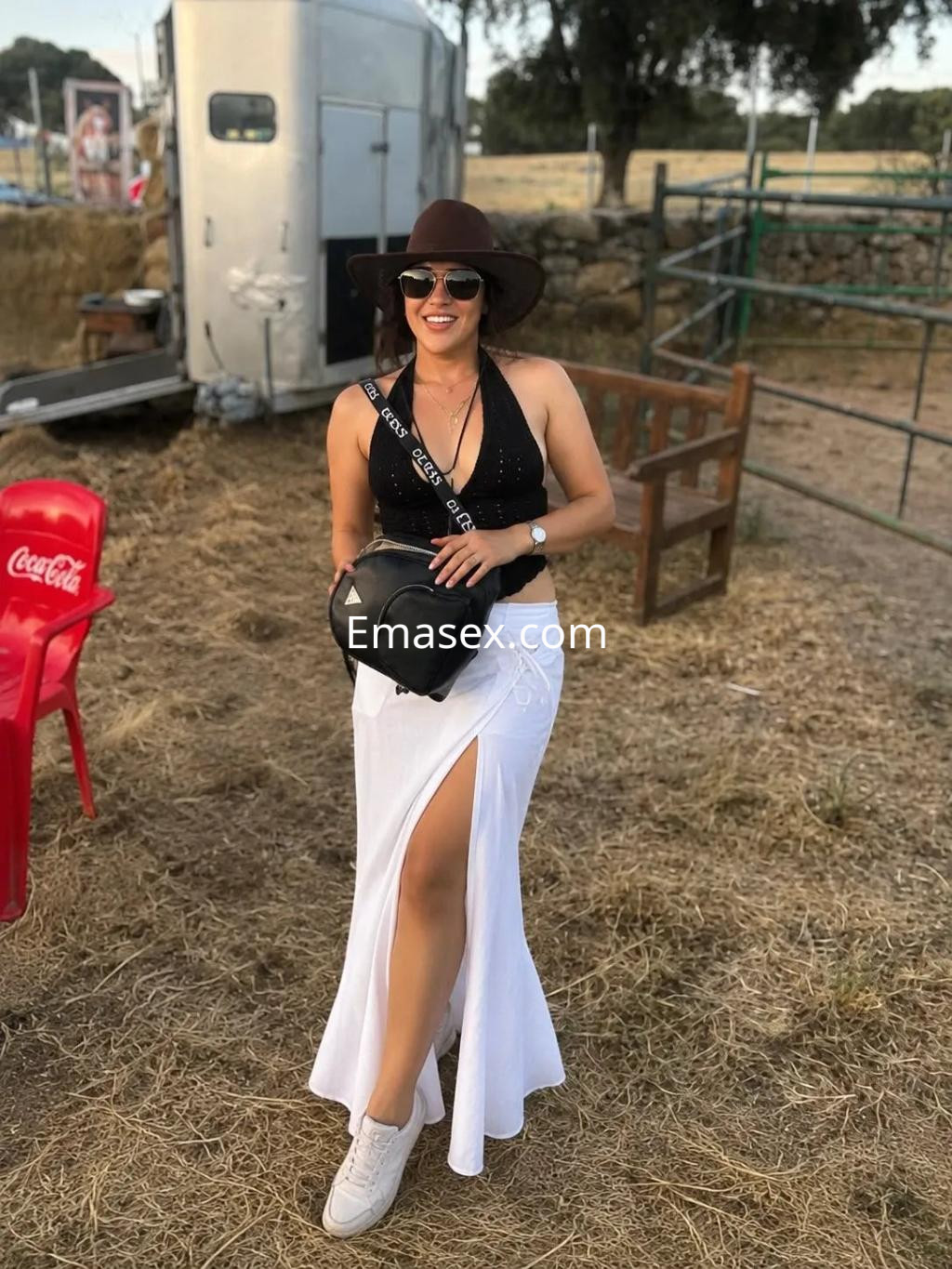 La puta viste un top negro y una falda blanca con una abertura, posando en un entorno rural en Palma de Mallorca.