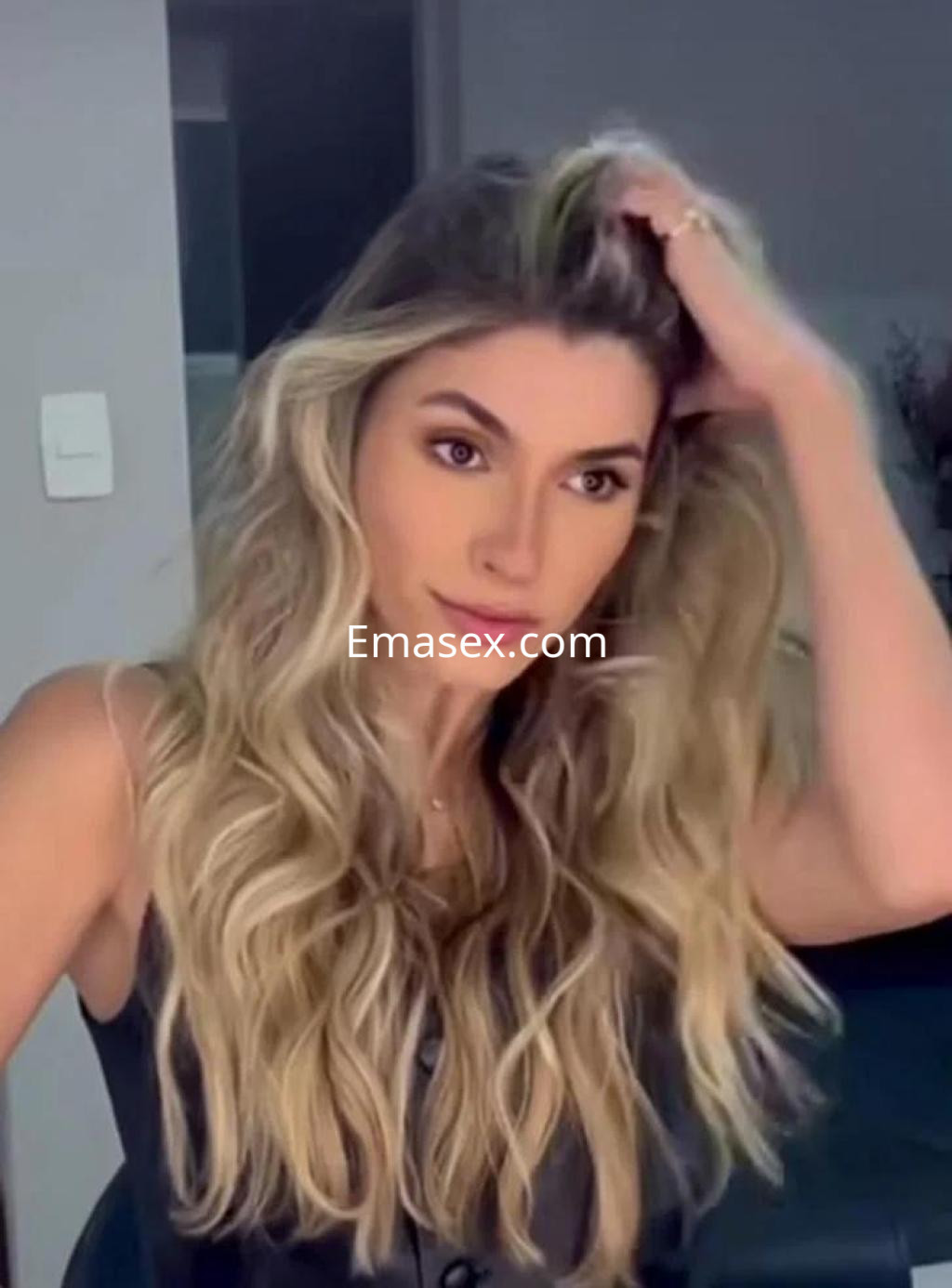 La puta de Palma de Mallorca luce un cabello largo y ondulado, con una blusa oscura, en un ambiente moderno.