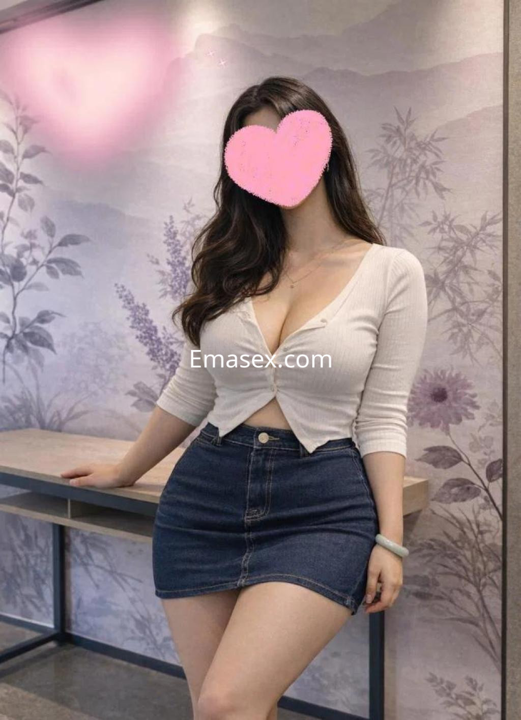 Puta con blusa blanca ajustada y falda corta de mezclilla, posando en un entorno moderno de Barcelona.