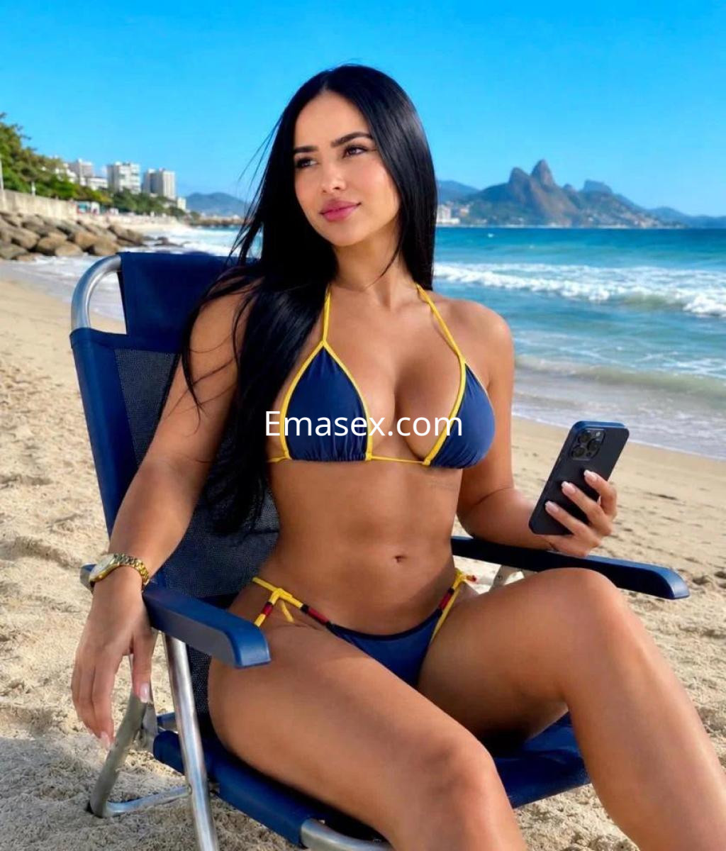Escort en Barcelona, sentada en una silla de playa, luciendo un bikini azul y amarillo, con cabello largo y lacio.
