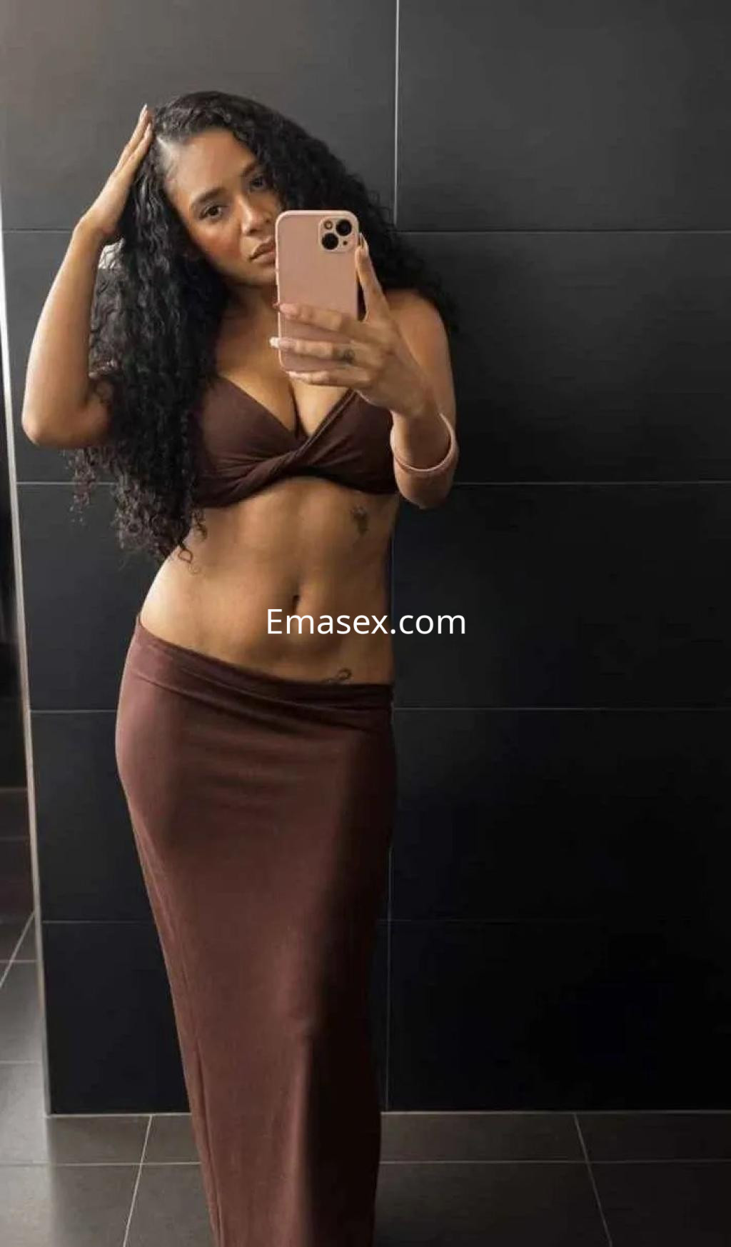 Escort en Sevilla con cabello rizado y oscuro, viste un conjunto marrón que resalta su figura.
