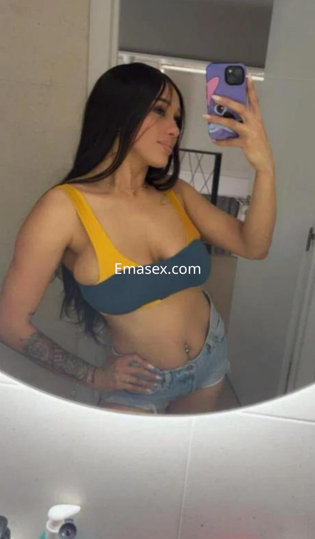 La puta en Barcelona posa con un top de dos colores y shorts de mezclilla, reflejándose en un espejo.