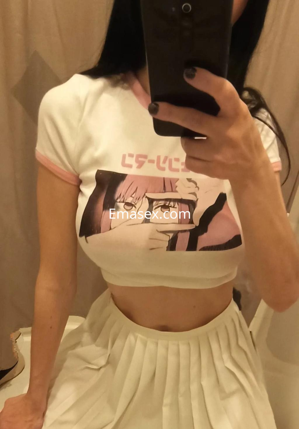 La puta en Alicante lleva una camiseta corta con un diseño gráfico y una falda blanca plisada.