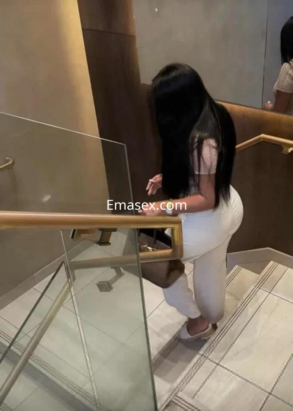 Escort en Alicante bajando una escalera, vistiendo una blusa clara y pantalones ajustados, con cabello largo y oscuro.