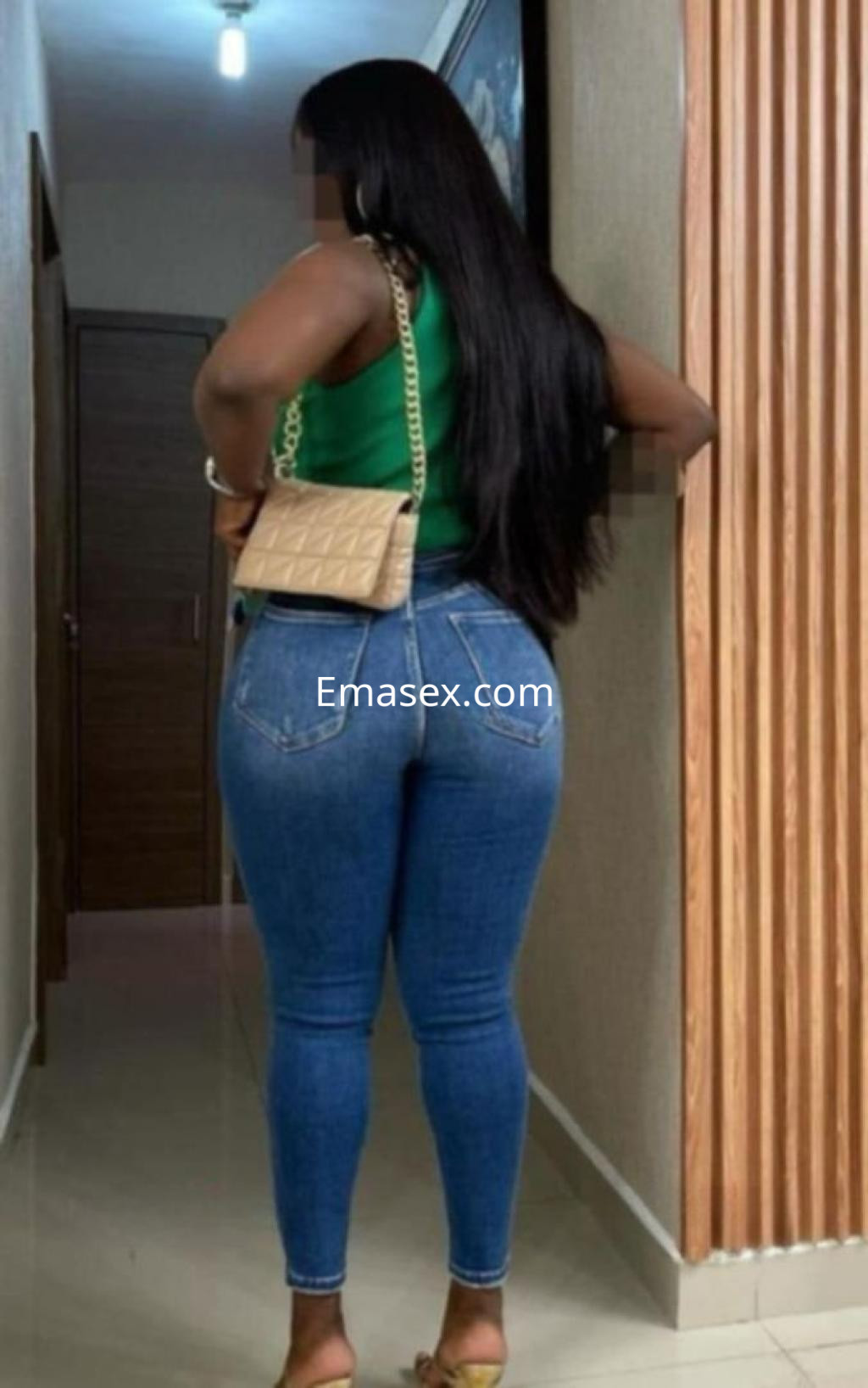 Escort con cabello largo y lacio, viste una blusa verde y jeans ajustados, posando en un pasillo en Almería.