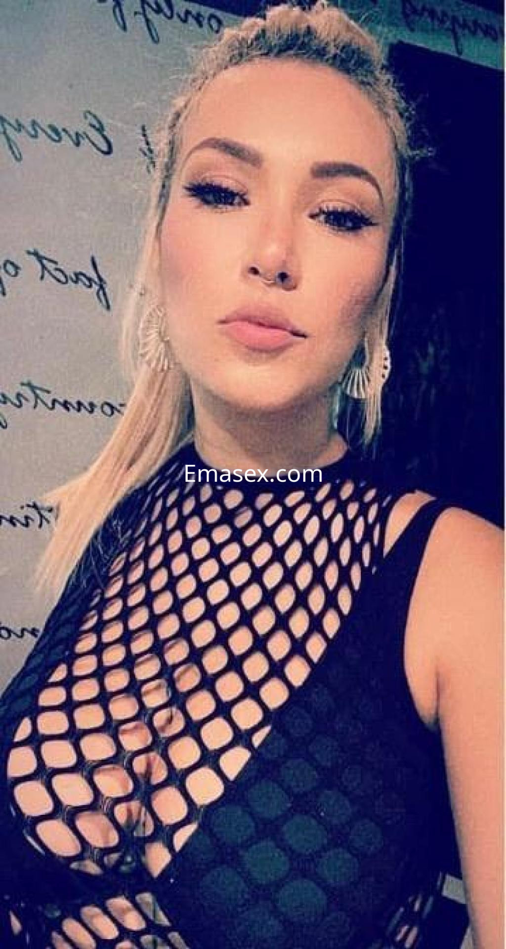 Escort en Barcelona con cabello rubio y recogido, luciendo un top de malla negra y pendientes llamativos.