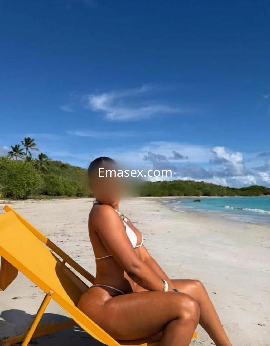 Escort en Cádiz sentada en una tumbona amarilla, con un bikini blanco, frente a una playa soleada.