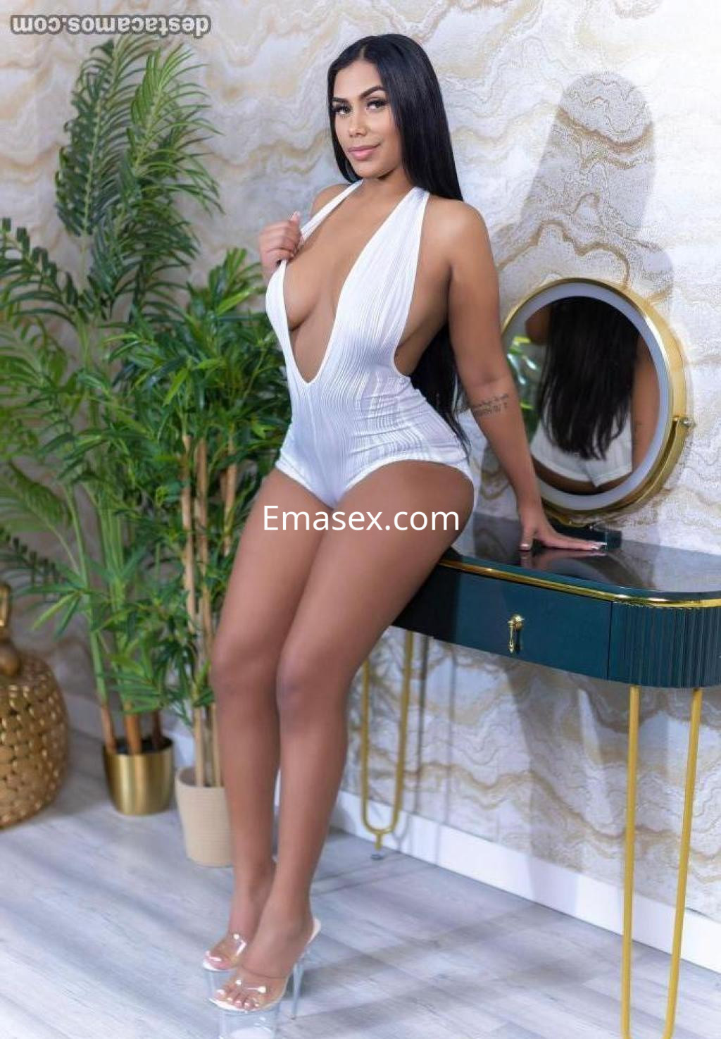 Puta posando en Madrid con un traje de baño blanco, tacones transparentes y cabello largo, frente a un espejo.