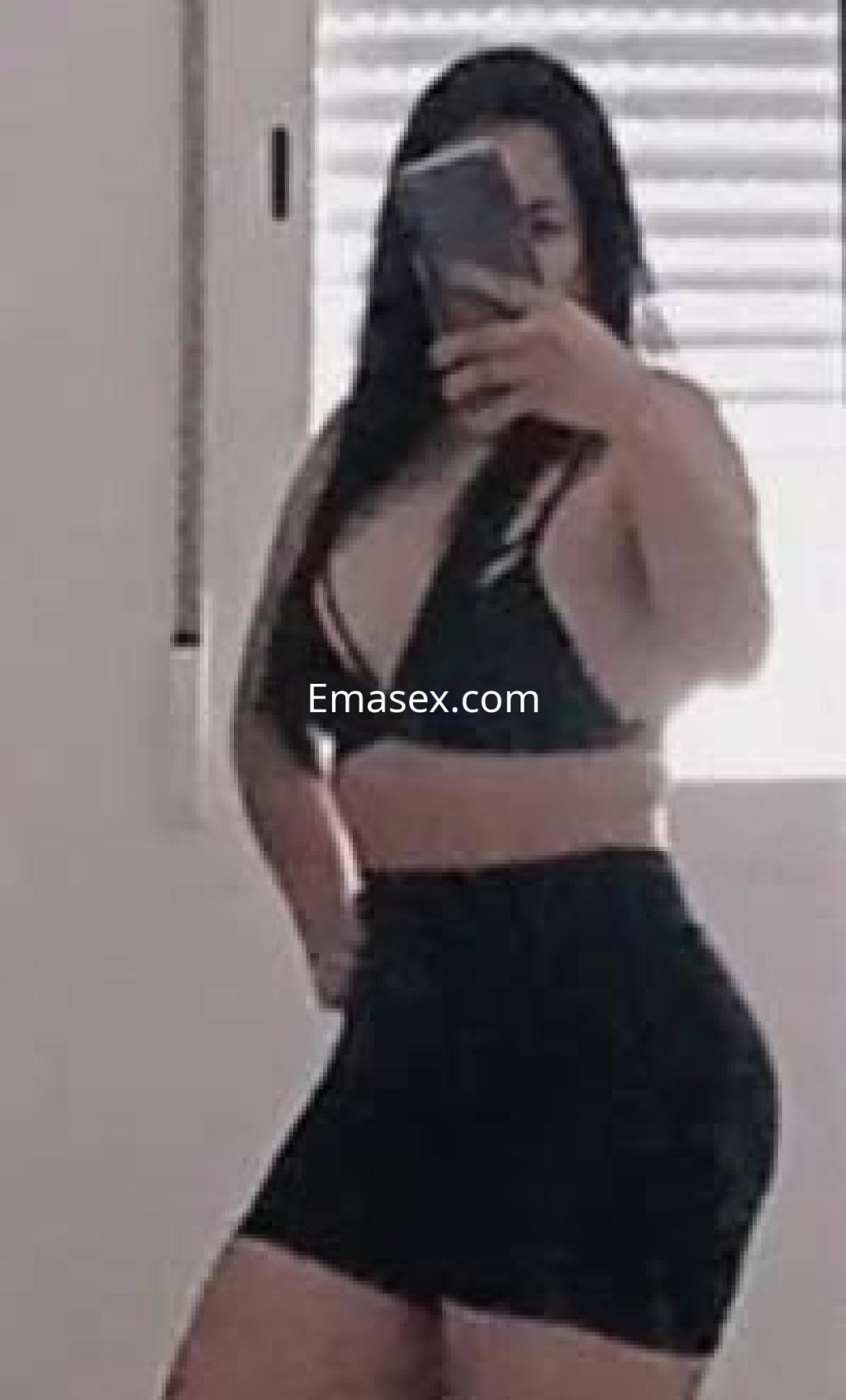 Escort en Madrid posando con un top negro y una falda corta, mostrando su silueta en un espejo.