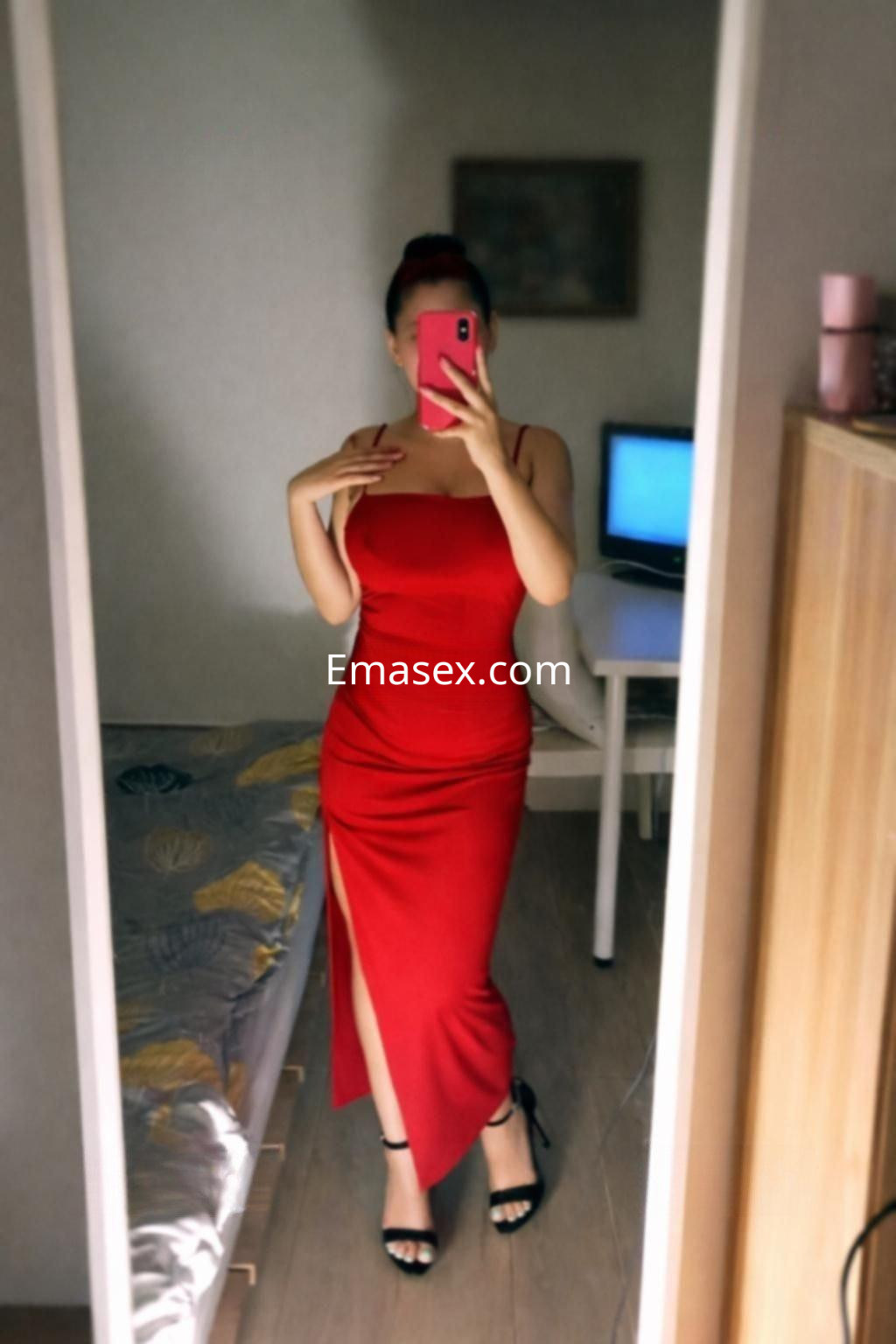 La puta lleva un vestido rojo ajustado con una abertura lateral, posando frente a un espejo en Madrid.