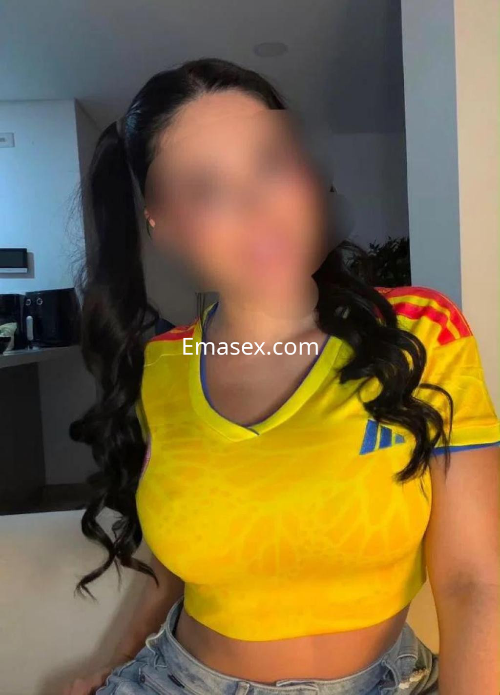 Escort en Las Palmas con cabello largo y ondulado, vistiendo una camiseta amarilla y shorts de mezclilla.