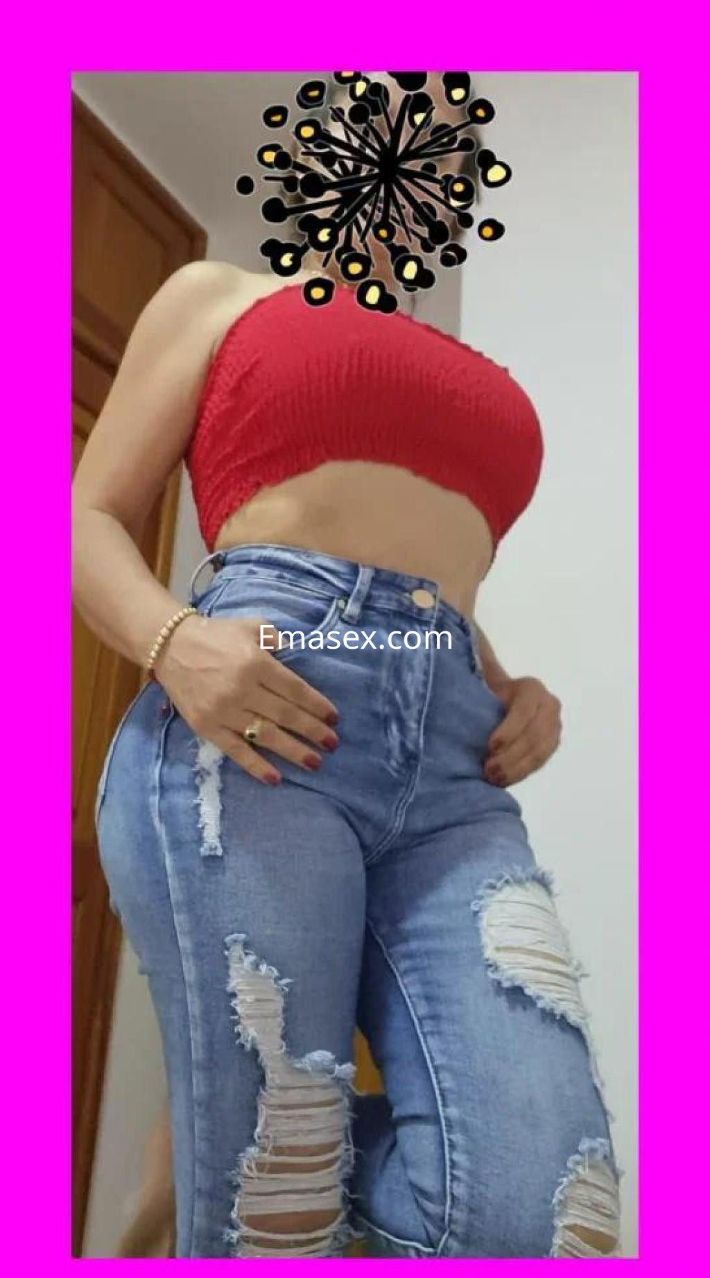 Puta en Pontevedra con top rojo y jeans rasgados, mostrando una pose ajustada y segura en un entorno interior.
