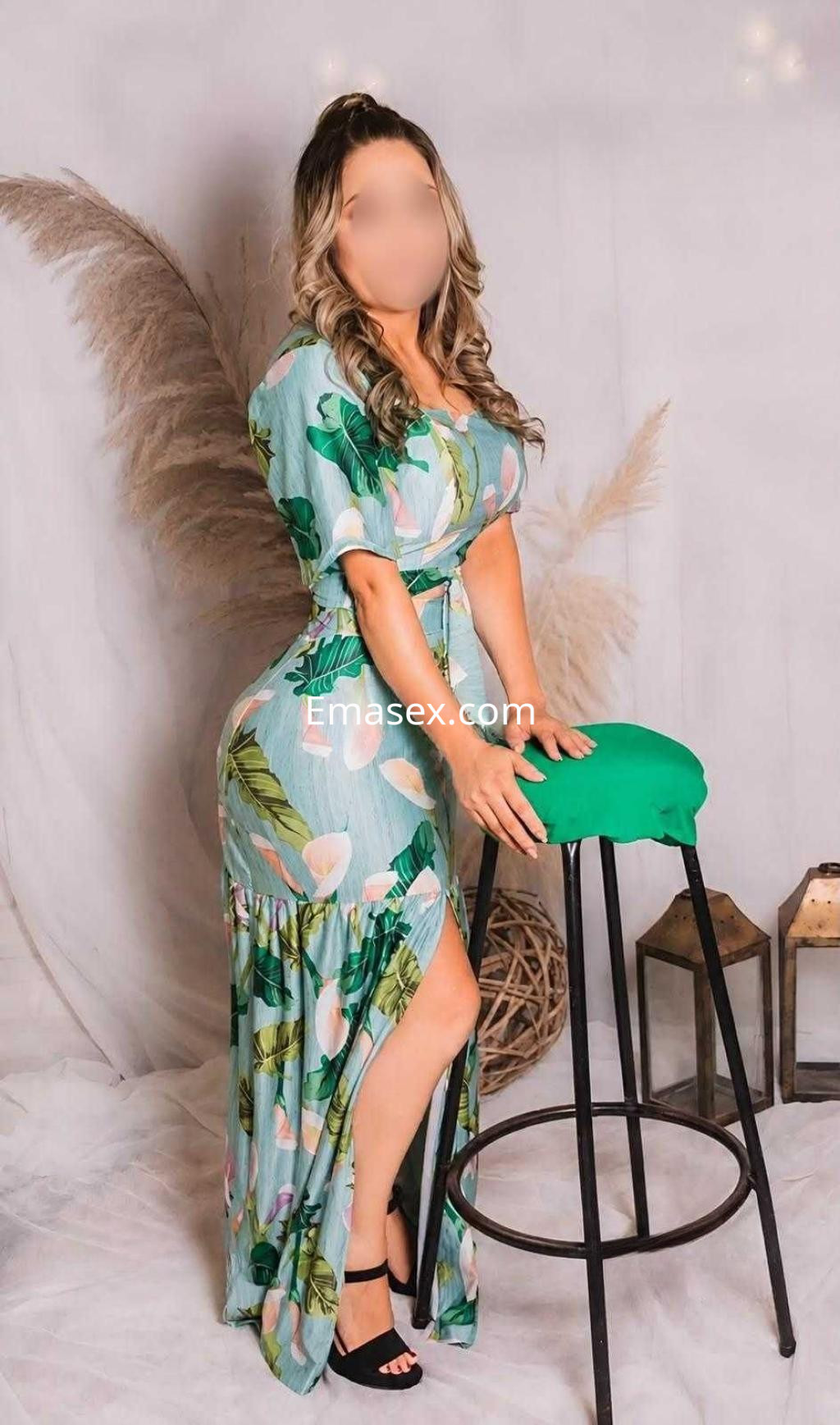 Escort posando de lado en Toledo, vistiendo un vestido largo floral con abertura, en un ambiente elegante.